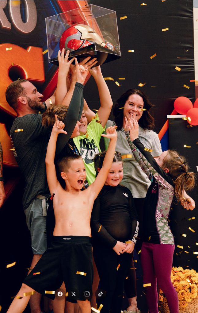 Young athletes and families celebrating with the champion trophy under gold confetti